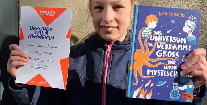 Anna Milena Meckbach hat dieses Jahr für das Fichte-Gymnasium am Stadtentscheid des Vorlesewettbewerbs teilgenommen und präsentiert stolz ihre Urkunde und ihr neues Buch.
